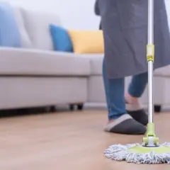 Persona con delantal y zapatillas limpiando el suelo con una mopa. Aprende como limpiar la mopa después de usarla para mantener tu hogar impecable.