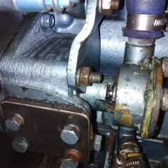Detalle de una bomba de agua que pierde agua, con óxido y corrosión visibles en sus componentes metálicos y mangueras.