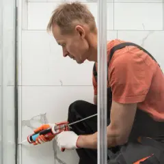 Hombre con guantes aplica sellador para plato de ducha.