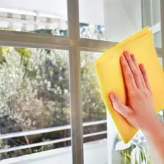 Mano limpiando un cristal con un paño amarillo para aprender como limpiar los cristales de las ventanas sin dejar marcas.