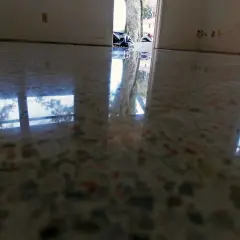 Reflejos en suelo de terrazo pulido, mostrando la entrada a una casa con bolsas de basura y un árbol. Se observa humedad en suelo de terrazo.
