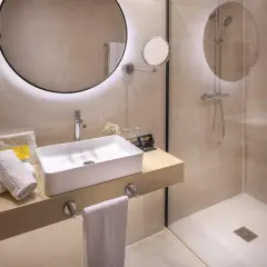 Baño moderno con lavabo sobre encimera y **ducha con suelo de obra**. Toallas blancas y dispensadores de jabón a la vista.