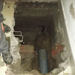 Excavación en el suelo de una vivienda para acceder a una arqueta con tuberías. Se ven restos de ladrillo y tierra.