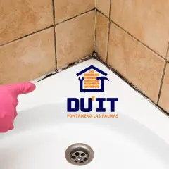 Mano con guante rosa señalando moho en juntas de baño. ¿Cómo sellar un baño? DU'IT Fontanero Las Palmas.