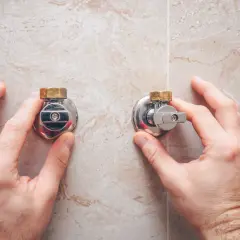 Manos ajustando dos llaves de agua. La palanca de la llave de la derecha está girada hacia abajo, indicando que se cierra hacia ese lado.