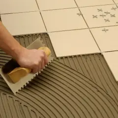 Mano extendiendo cemento cola con llana para poner azulejos.