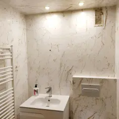 Elegante baño con paredes y techo acabados en resina epoxi con veteado marrón sobre blanco. Incluye lavabo, toallero y cisterna empotrada.