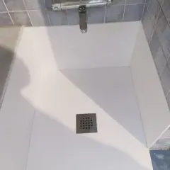 Instalación de un nuevo plato de ducha blanco, con azulejos azules y grifería cromada.