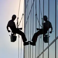 Siluetas de operarios realizando limpieza de cristales en edificios y locales, suspendidos por cuerdas.