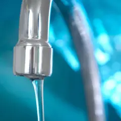 Grifo cromado con chorro de agua, indicando un buen bar presión de agua. Fondo azul brillante.