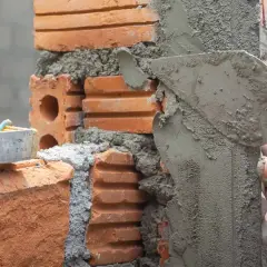 Man applying mezcla para pegar ladrillos con una paleta. Se ve una regla de albañil.