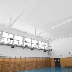 Techo de gimnasio con falso techo Heraklith, ventanas altas, canasta de baloncesto y equipamiento deportivo.