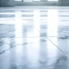 Suelo de mármol pulido con vetas grises. La luz se refleja intensamente, mostrando que el mármol es poroso y absorbe la humedad.
