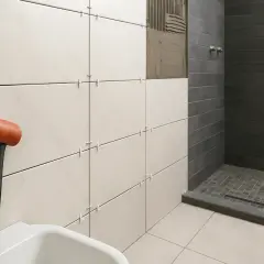 Alicatar baño: martillo de goma junto a azulejos blancos y grises en proceso de instalación.