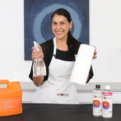Mujer sonriente muestra cómo limpiar la resina epoxi de los utensilios con spray y papel.