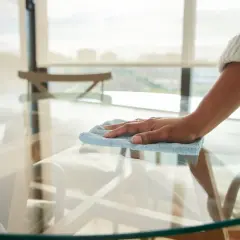Mano limpiando una mesa de cristal, eliminando los cristales opacos para dejarla reluciente.