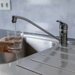 Un vaso se llena de agua bajo un grifo moderno, mostrando la buena presión del agua del grifo.