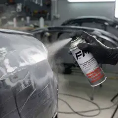 Mano enguantada aplica imprimación en spray a un coche. Se puede dar imprimación encima de pintura para un acabado perfecto.