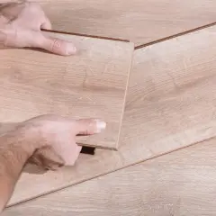 Man's hands fitting a new laminate plank to replace damaged parquet.