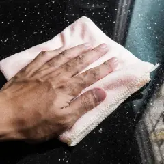 Mano limpiando manchas de humedad en mármol negro con un paño rosa.