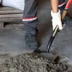 Mano enguantada usa pala para mezclar mortero cemento fresco en el suelo.