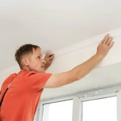 Hombre instalando moldura de escayola en el techo. Aprende como hacer escayola para techo y embellece tu hogar.