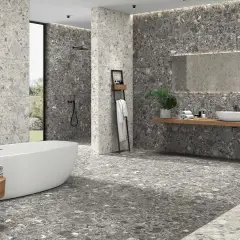 Baño moderno con bañera exenta y lavabo sobre encimera. Las paredes y el suelo muestran diferentes tipos de azulejos con efecto terrazo en tonos grises.