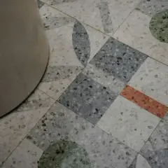 Detalle de un suelo terrazo con diseño geométrico y un pilar. El pulido del suelo terrazo resalta sus motas de colores.
