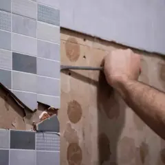 Persona usando un cincel para quitar juntas de azulejos viejos y dañados de una pared.