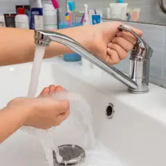 Mano ajustando el grifo para aumentar la presión del agua mientras se lava las manos en un lavabo blanco.