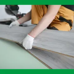 Manos enguantadas instalando suelos gran formato de madera gris.