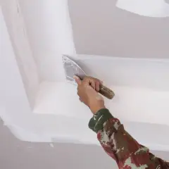 Mano aplica masilla con espátula en el techo, como quitar escayola del techo.