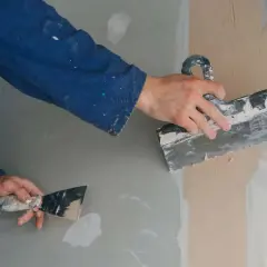 Man alicatando sobre pladur, alisando la pared con una llana.