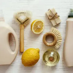 Dos botellas de detergente, jabón, limones y cepillos de madera para una limpieza sostenible.