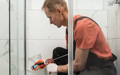 Hombre con guantes aplica sellador para plato de ducha.