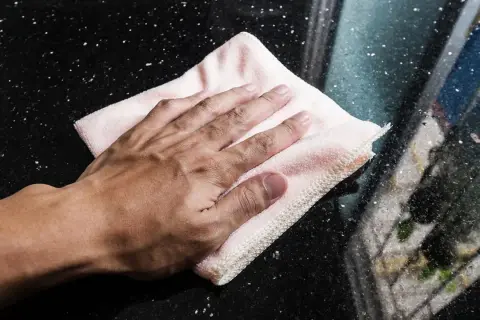 Mano limpiando manchas de humedad en mármol negro con un paño rosa.