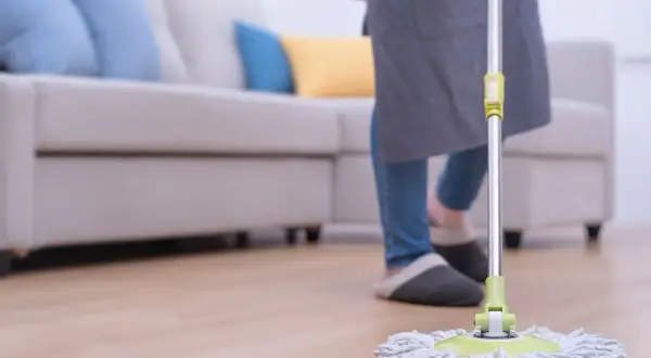 Persona con delantal y zapatillas limpiando el suelo con una mopa. Aprende como limpiar la mopa después de usarla para mantener tu hogar impecable.