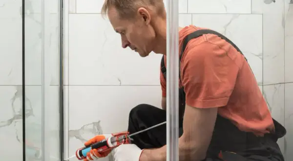 Hombre con guantes aplica sellador para plato de ducha.