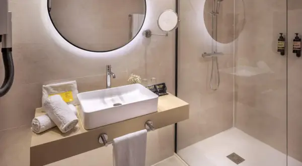Baño moderno con lavabo sobre encimera y **ducha con suelo de obra**. Toallas blancas y dispensadores de jabón a la vista.