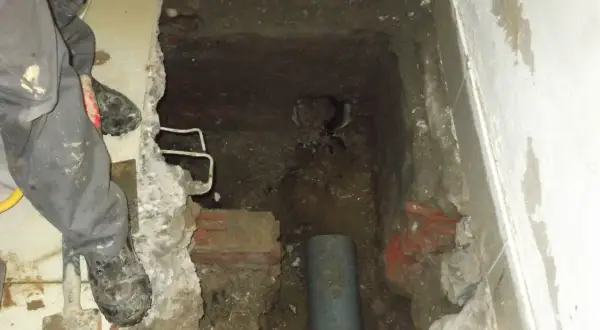 Excavación en el suelo de una vivienda para acceder a una arqueta con tuberías. Se ven restos de ladrillo y tierra.