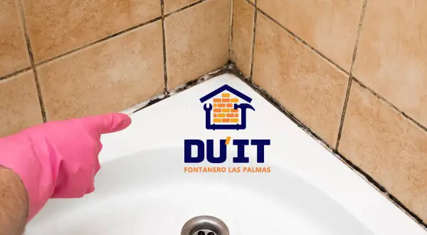 Mano con guante rosa señalando moho en juntas de baño. ¿Cómo sellar un baño? DU'IT Fontanero Las Palmas.