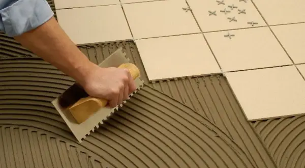 Mano extendiendo cemento cola con llana para poner azulejos.