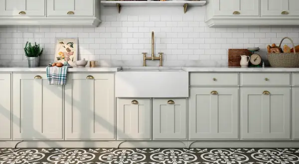 Cocina con suelo hidráulico de diseño floral. Encimera de mármol, fregadero blanco, grifería dorada y armarios claros.