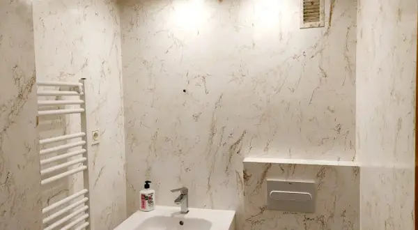 Elegante baño con paredes y techo acabados en resina epoxi con veteado marrón sobre blanco. Incluye lavabo, toallero y cisterna empotrada.