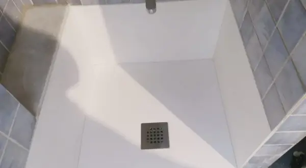 Instalación de un nuevo plato de ducha blanco, con azulejos azules y grifería cromada.