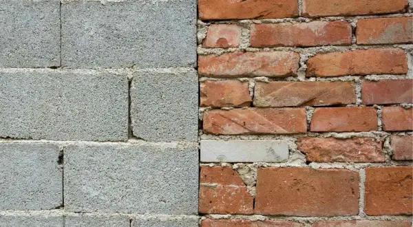 Muro de bloques de hormigón gris a la izquierda, ladrillos rojos desgastados a la derecha.