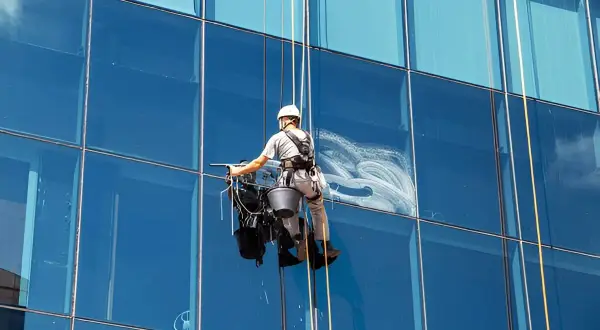 Trabajador en arnés limpiando cristales altos de un edificio moderno.