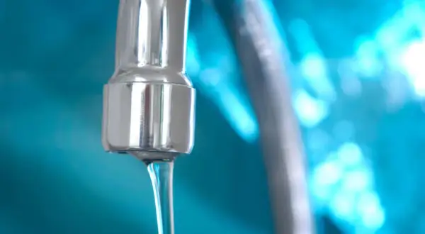 Grifo cromado con chorro de agua, indicando un buen bar presión de agua. Fondo azul brillante.