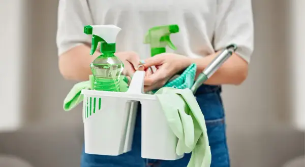Persona con kit de limpieza: guantes, botellas rociadoras y paños. Las funciones de un auxiliar de limpieza son variadas.
