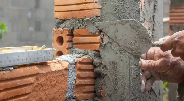Man applying mezcla para pegar ladrillos con una paleta. Se ve una regla de albañil.